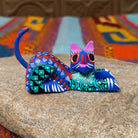 Reclining Oaxacan cat wood carving with a curled tail, oversized eyes, and colorful hand-painted geometric patterns.