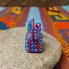 Reclining Oaxacan cat wood carving with a curled tail, oversized eyes, and colorful hand-painted geometric patterns.