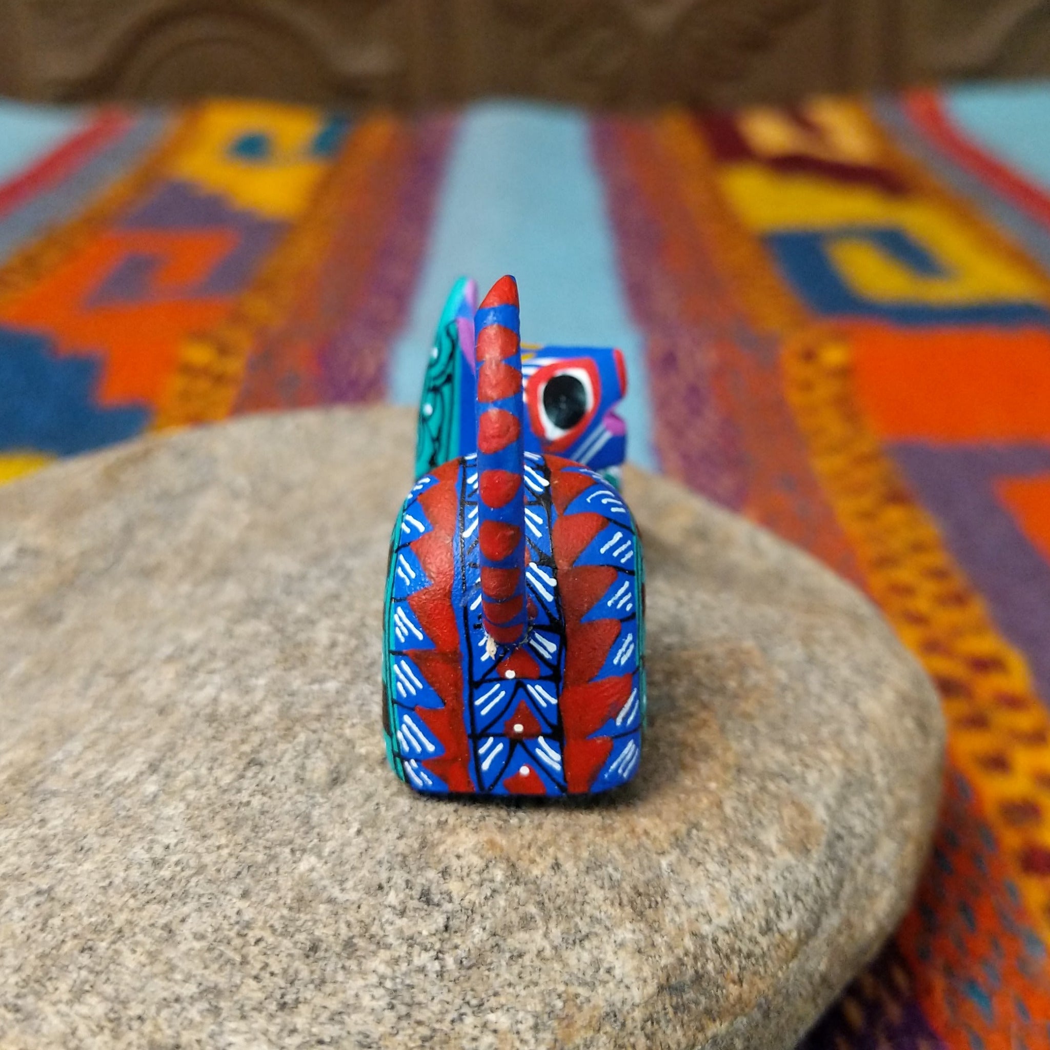Reclining Oaxacan cat wood carving with a curled tail, oversized eyes, and colorful hand-painted geometric patterns.