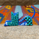Reclining Oaxacan cat wood carving with a curled tail, oversized eyes, and colorful hand-painted geometric patterns.