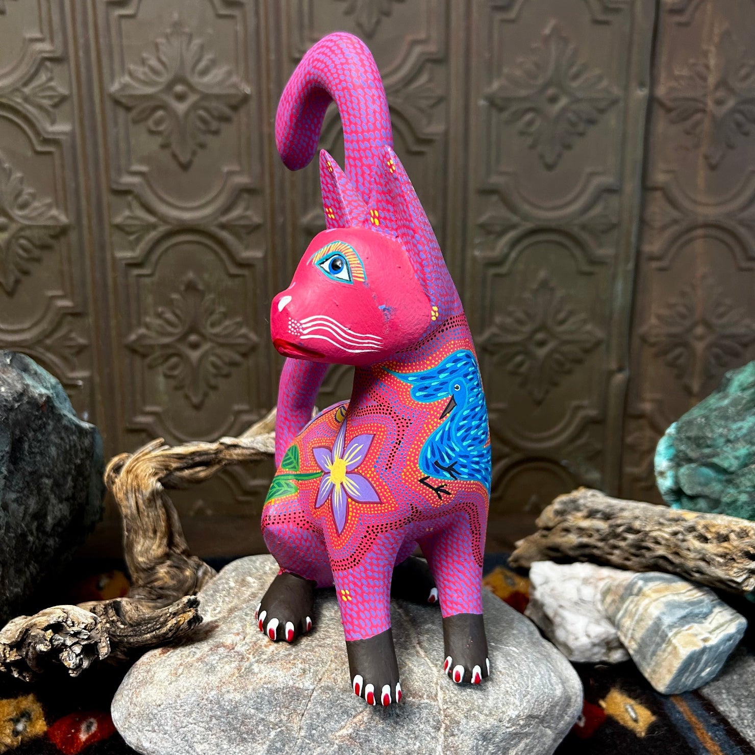 Pink cat figurine with large blue eyes, adorned with purple and yellow floral patterns across its chest.