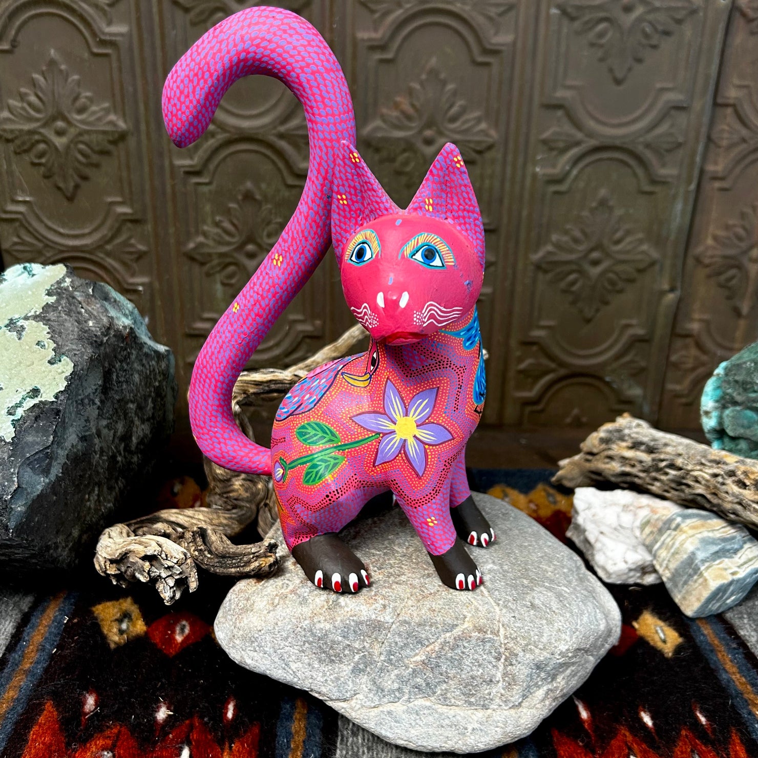 Pink cat figurine with large blue eyes, adorned with purple and yellow floral patterns across its chest.