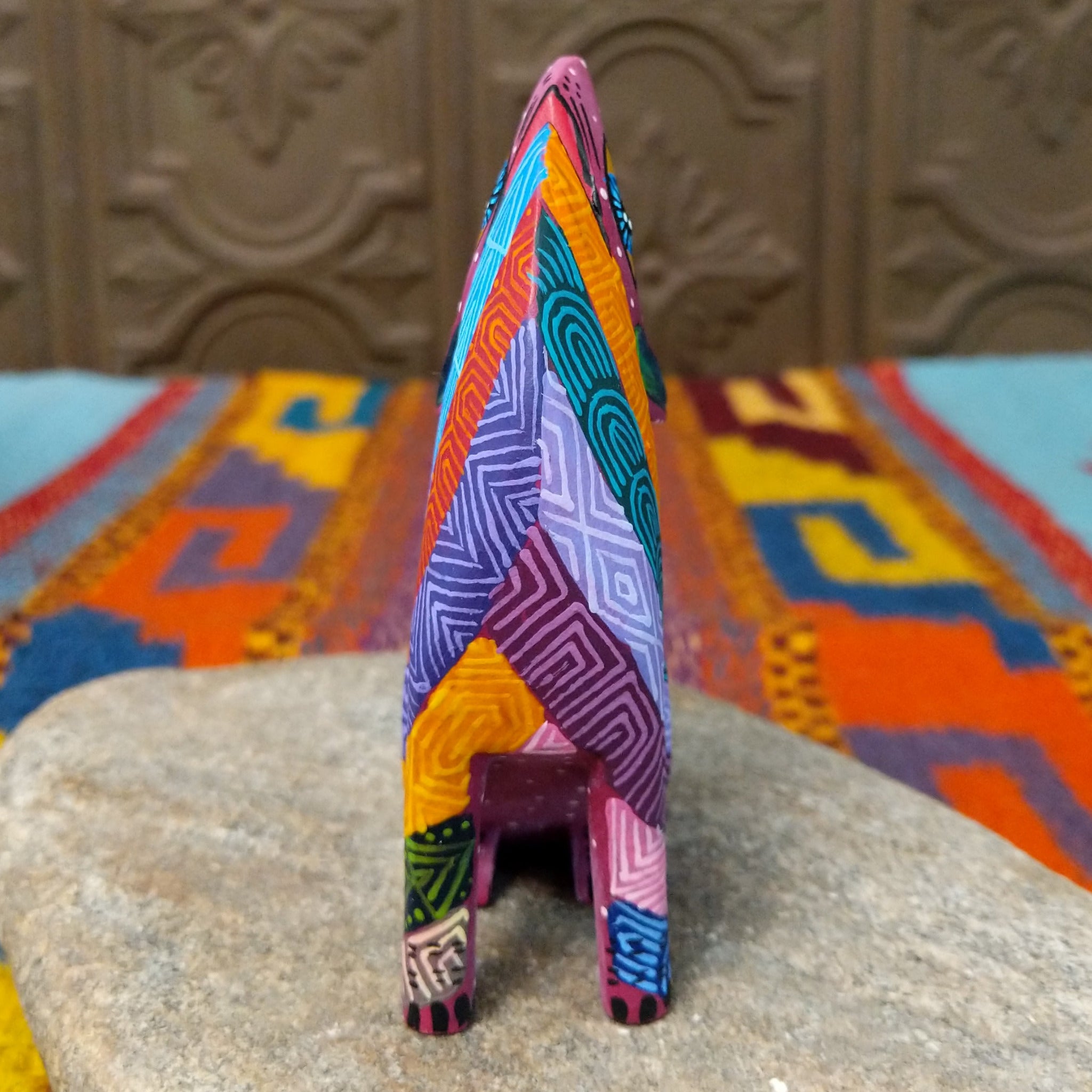 Oaxacan coyote wood carving by Julia Calvo Olivera with an arched body, raised muzzle, curled patterned tail, and colorful geometric designs.