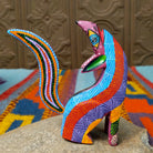Oaxacan coyote wood carving by Julia Calvo Olivera with an arched body, raised muzzle, curled patterned tail, and colorful geometric designs.