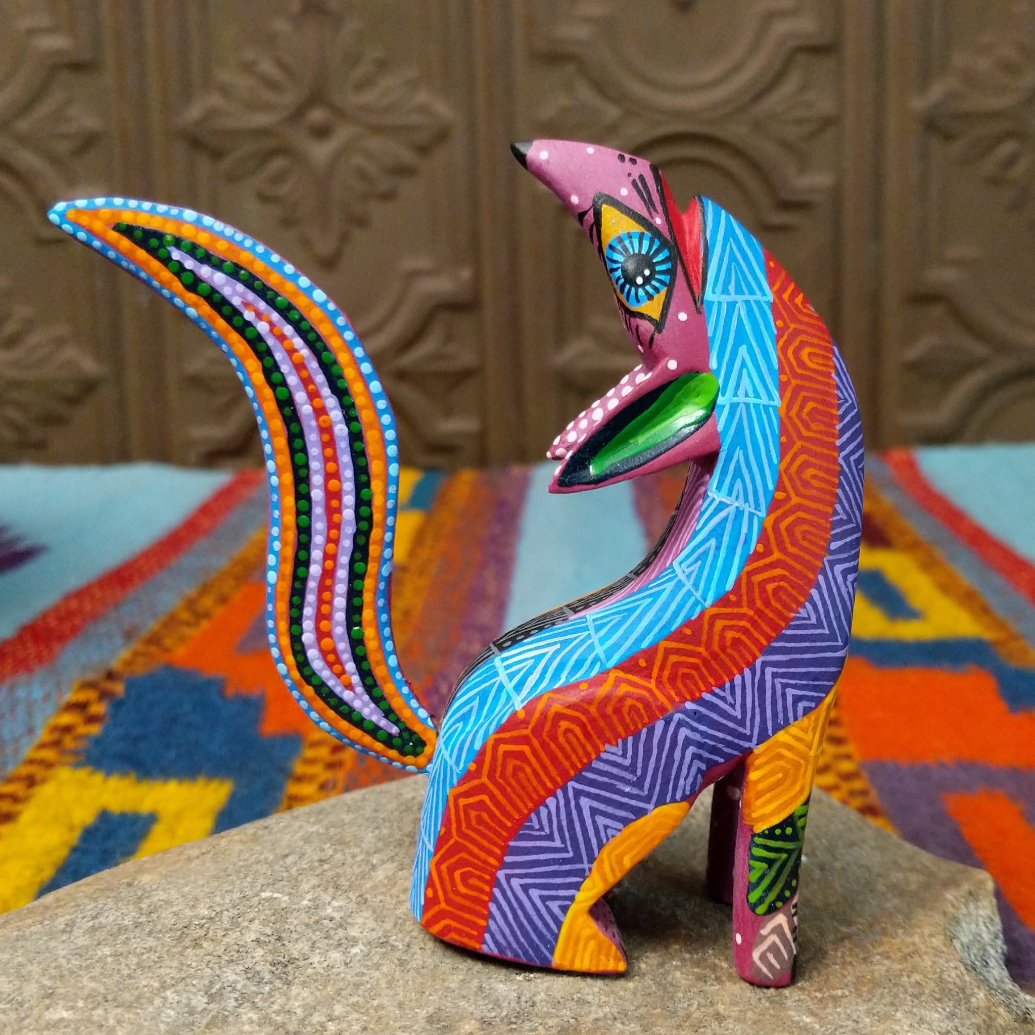 Oaxacan coyote wood carving by Julia Calvo Olivera with an arched body, raised muzzle, curled patterned tail, and colorful geometric designs.