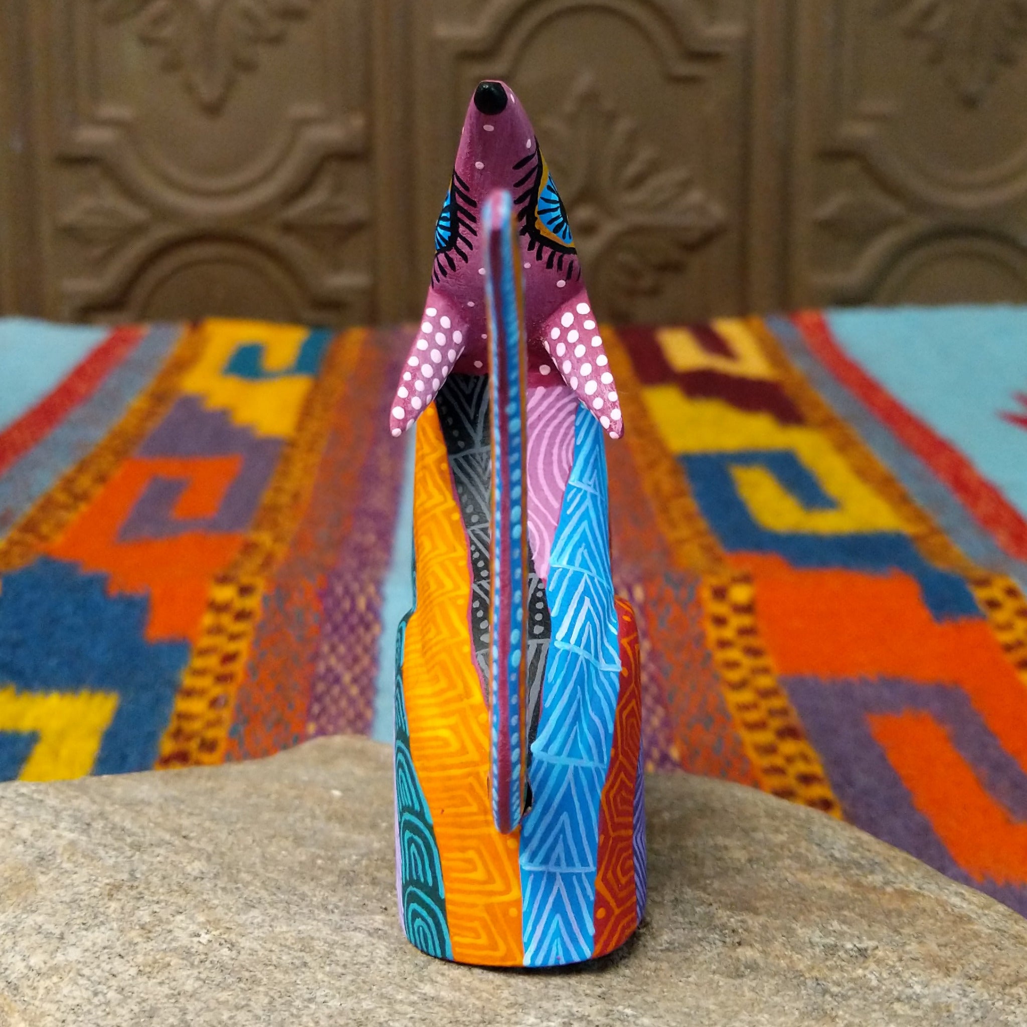 Oaxacan coyote wood carving by Julia Calvo Olivera with an arched body, raised muzzle, curled patterned tail, and colorful geometric designs.