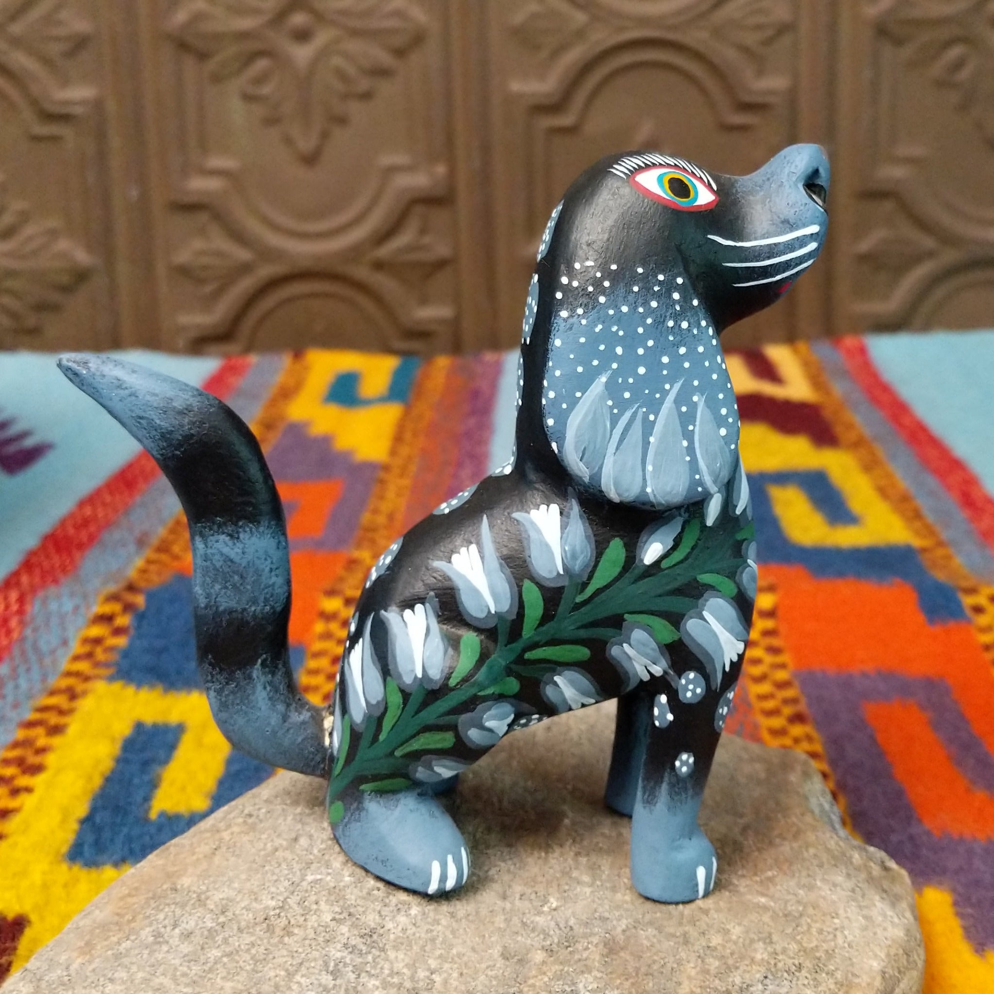 Oaxacan dog wood carving by Jose Olivera Perez with an open mouth, raised curved tail, and hand-painted floral and leafy designs.