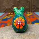 This green Oaxacan frog wood carving by Roberta Angeles features raised eyes, colorful dotted patterns, a red mouth, and long legs with oversized hand-painted webbed feet; rear view.
