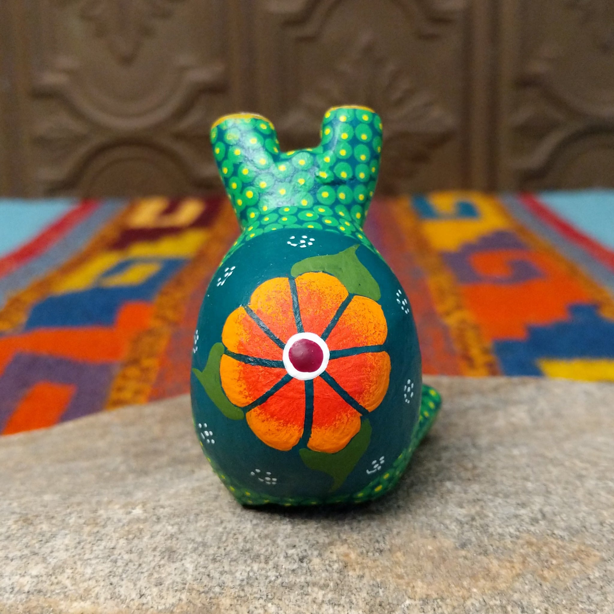 This green Oaxacan frog wood carving by Roberta Angeles features raised eyes, colorful dotted patterns, a red mouth, and long legs with oversized hand-painted webbed feet; rear view.