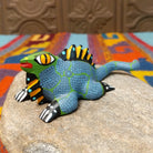 This colorful Oaxacan iguana wood carving features a green head, blue dotted body, golden eyes, black-and-yellow back spines, and a long patterned tail.