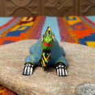 This colorful Oaxacan iguana wood carving features a green head, blue dotted body, golden eyes, black-and-yellow back spines, and a long patterned tail; front facing view.