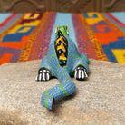 This colorful Oaxacan iguana wood carving features a green head, blue dotted body, golden eyes, black-and-yellow back spines, and a long patterned tail; rear view.