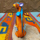 Oaxacan jaguar wood carving by Abundio Muñoz with an orange patterned body, blue legs, curled tail, and geometric painted details.