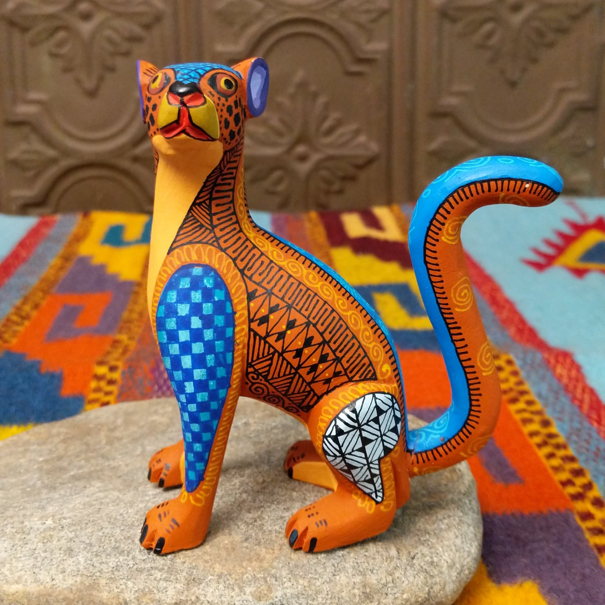 Oaxacan jaguar wood carving by Abundio Muñoz with an orange patterned body, blue legs, curled tail, and geometric painted details.