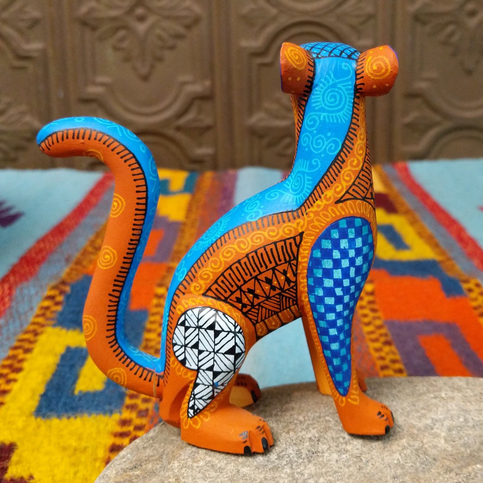 Oaxacan jaguar wood carving by Abundio Muñoz with an orange patterned body, blue legs, curled tail, and geometric painted details.