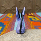 Oaxacan jerboa wood carving with oversized blue patterned ears, a lavender body, orange front legs, and long curved black tail.