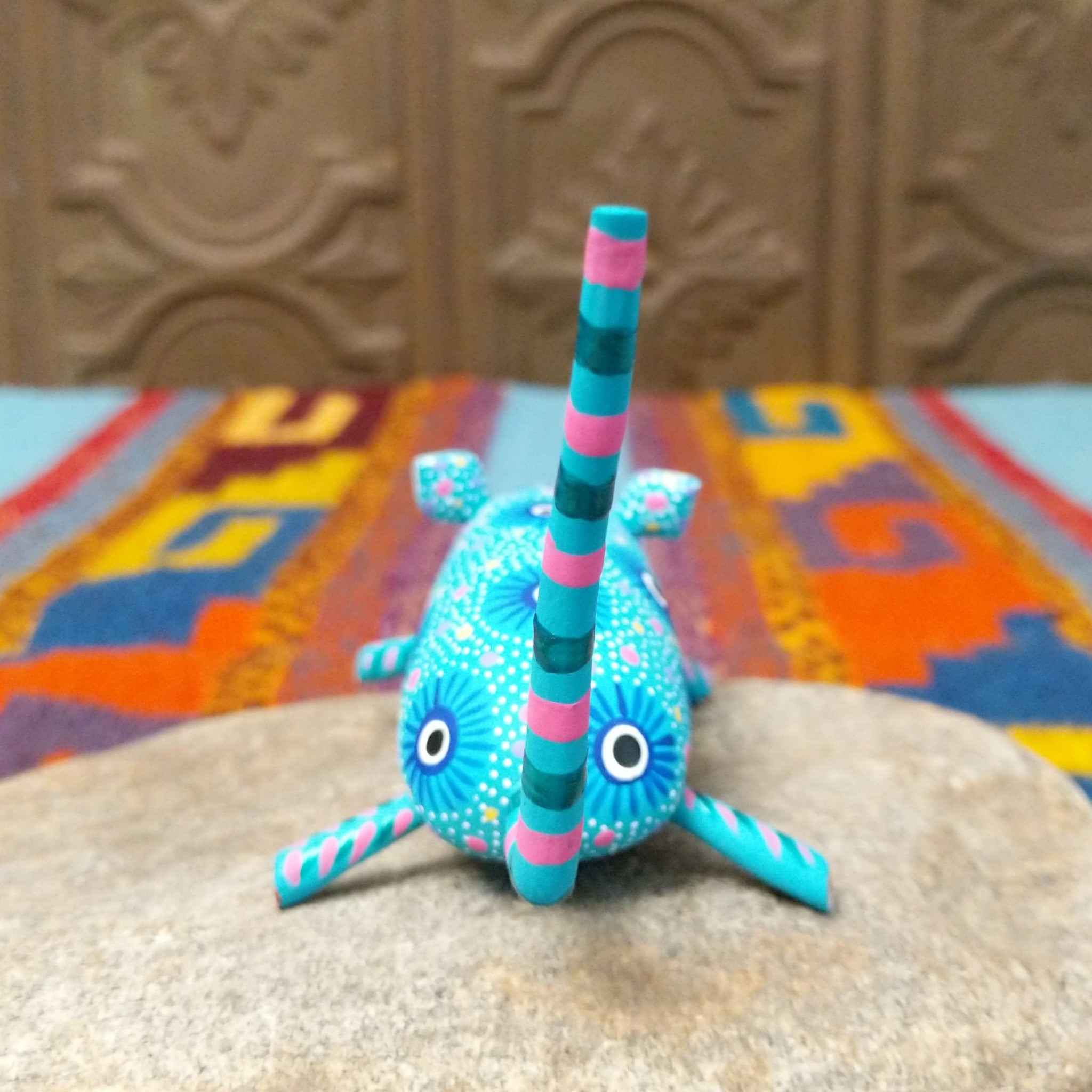 This turquoise Oaxacan mouse wood carving by Fabian Ramirez features colorful hand-painted patterns, pink-accented ears and legs, and a long striped tail; backside view.