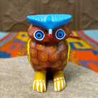 Oaxacan owl wood carving with a rounded body, large circular eyes, painted feather patterns, and a broad blue brow.