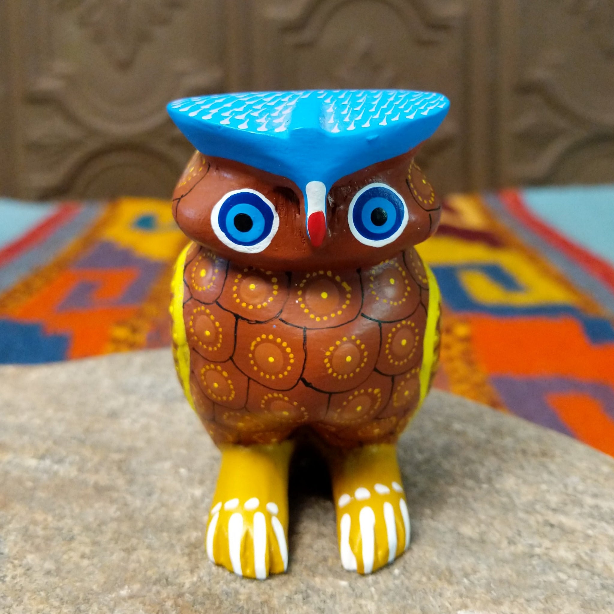 Oaxacan owl wood carving with a rounded body, large circular eyes, painted feather patterns, and a broad blue brow.