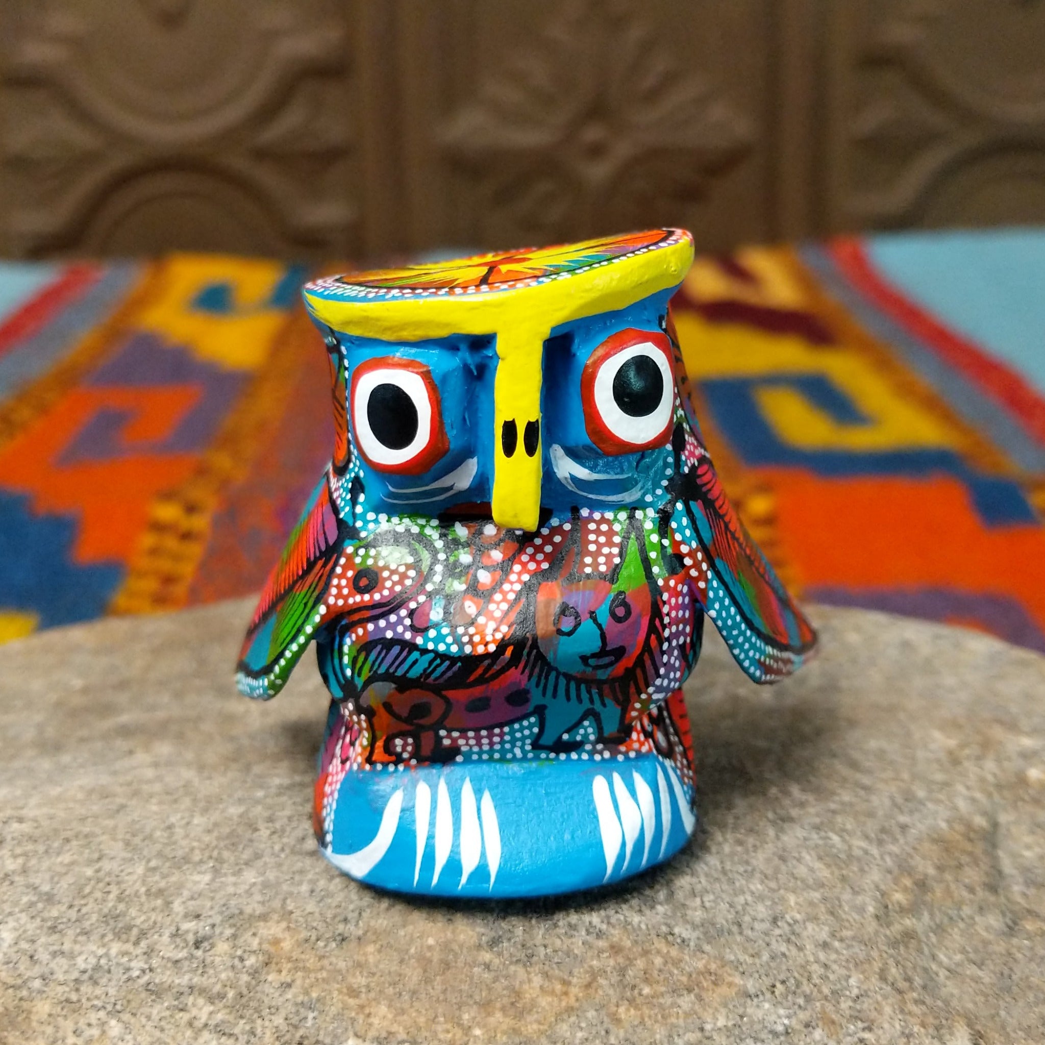 Oaxacan owl wood carving with oversized round eyes and a colorful patchwork of birds, leaves, dots, and abstract painted designs.