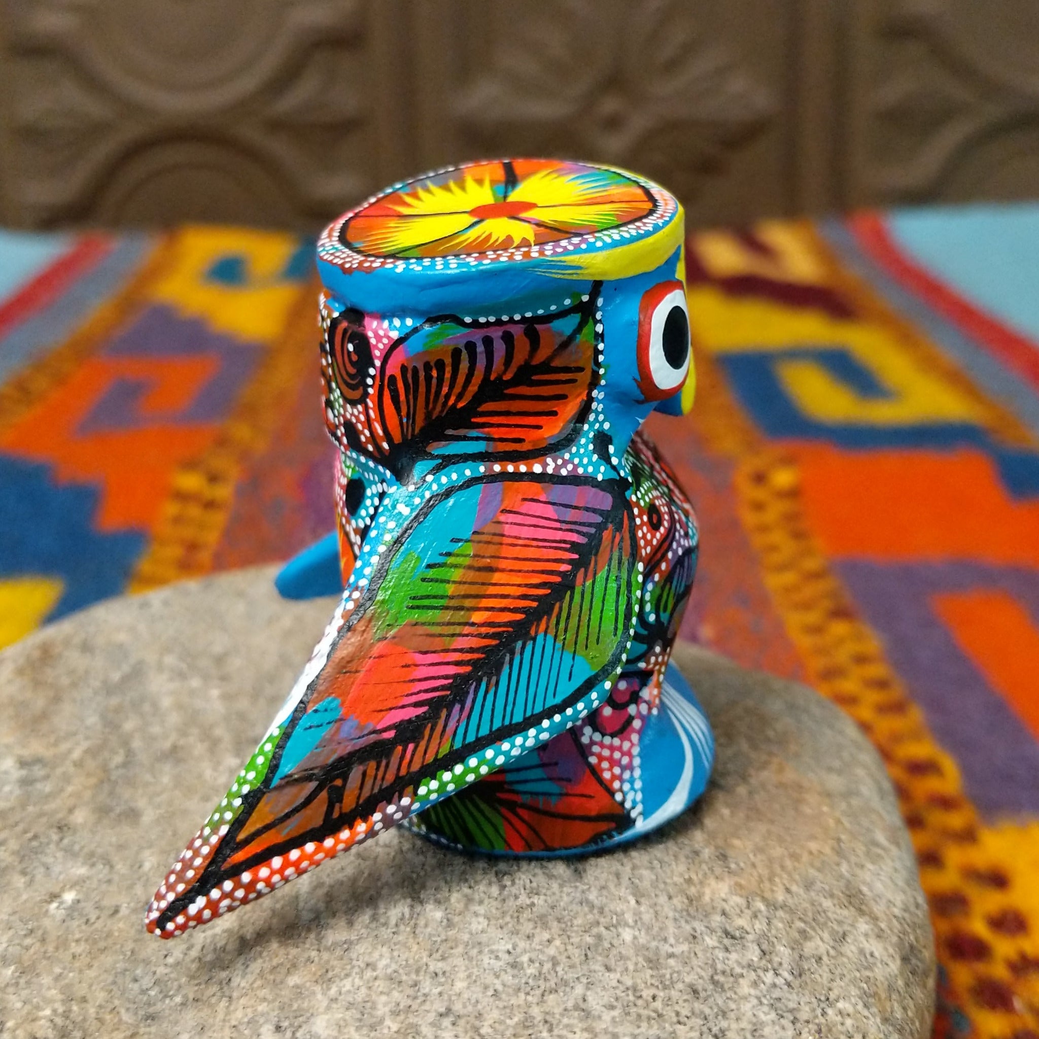 Oaxacan owl wood carving with oversized round eyes and a colorful patchwork of birds, leaves, dots, and abstract painted designs.