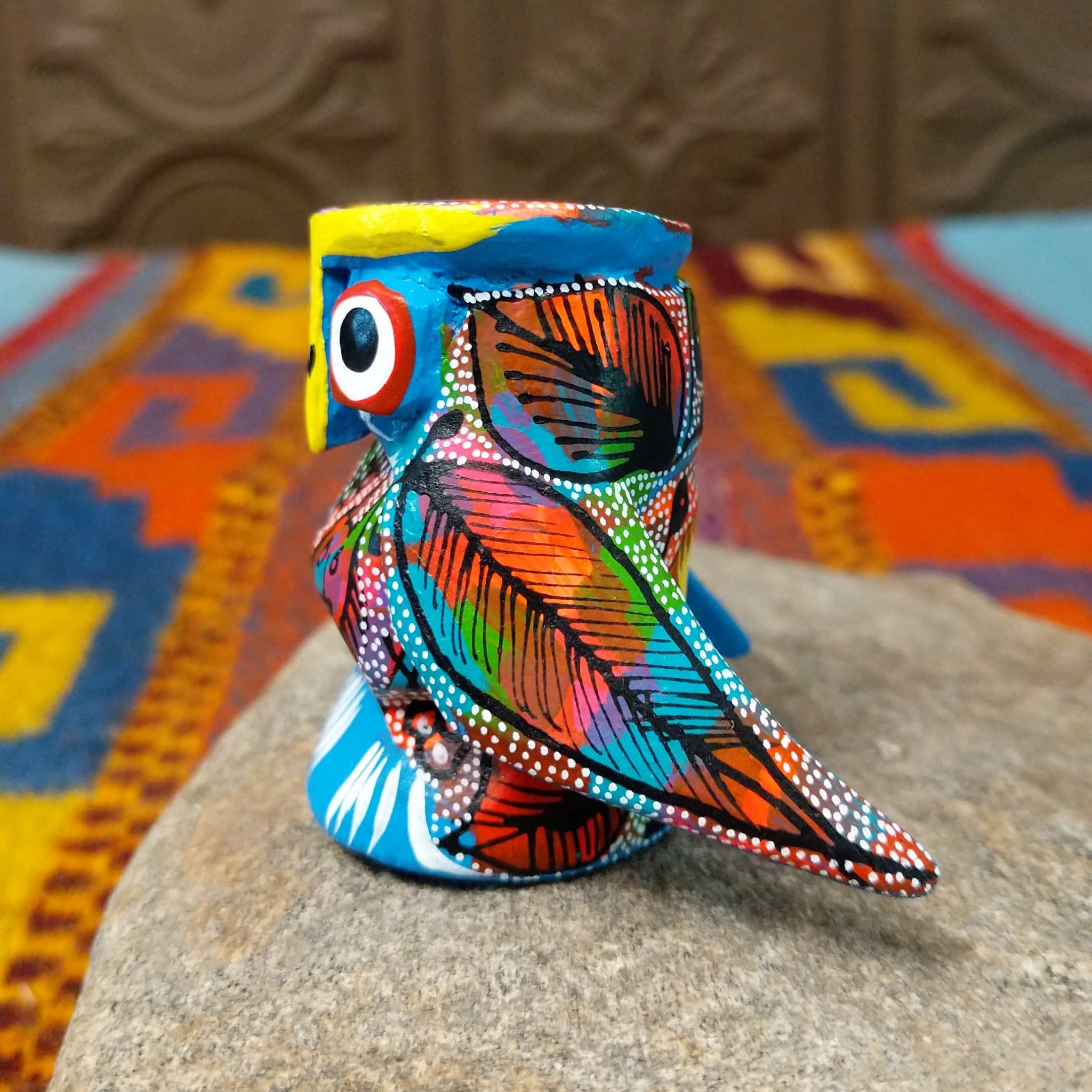 Oaxacan owl wood carving with oversized round eyes and a colorful patchwork of birds, leaves, dots, and abstract painted designs.