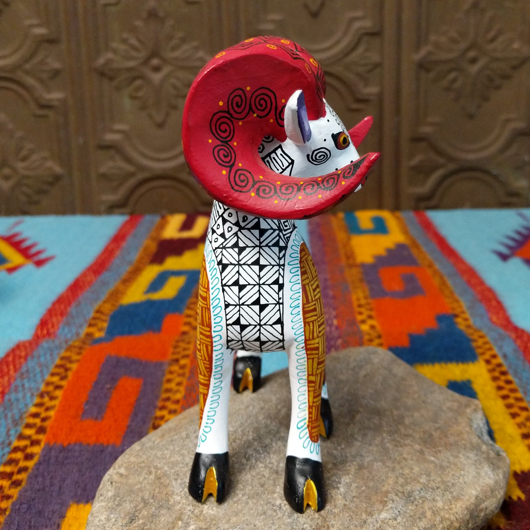 This Oaxacan ram wood carving by Abundia Munoz features large red curled horns, purple ears, a white body, and intricate black, orange, brown, and turquoise geometric patterns; side view.