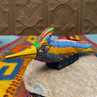 Oaxacan roadrunner wood carving by Julia Calvo Olivera with a long yellow beak, swept-back crest, and multicolored geometric patterns.