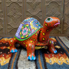 Orange wood tortoise carving with a green rim, featuring a large green eye and colorful floral shell patterns.
