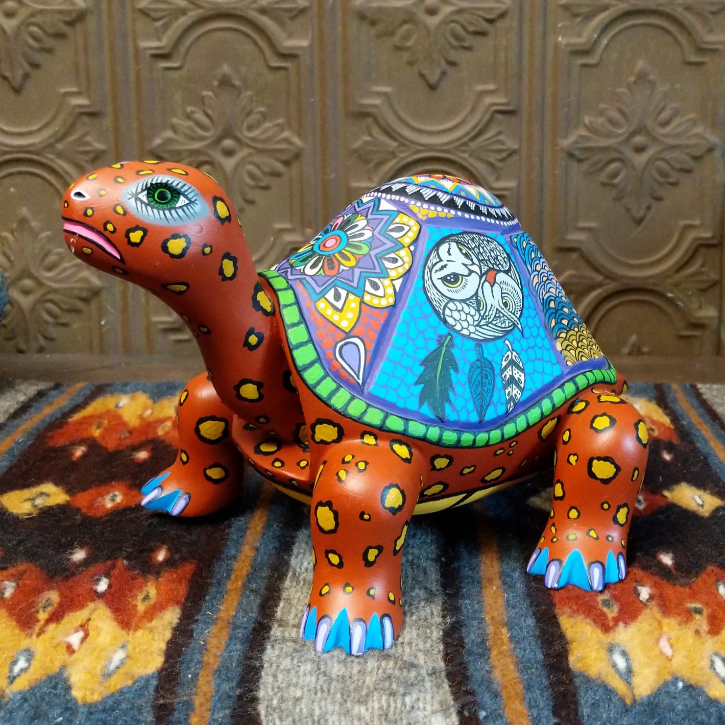Orange wood tortoise carving with a green rim, featuring a large green eye and colorful floral shell patterns.