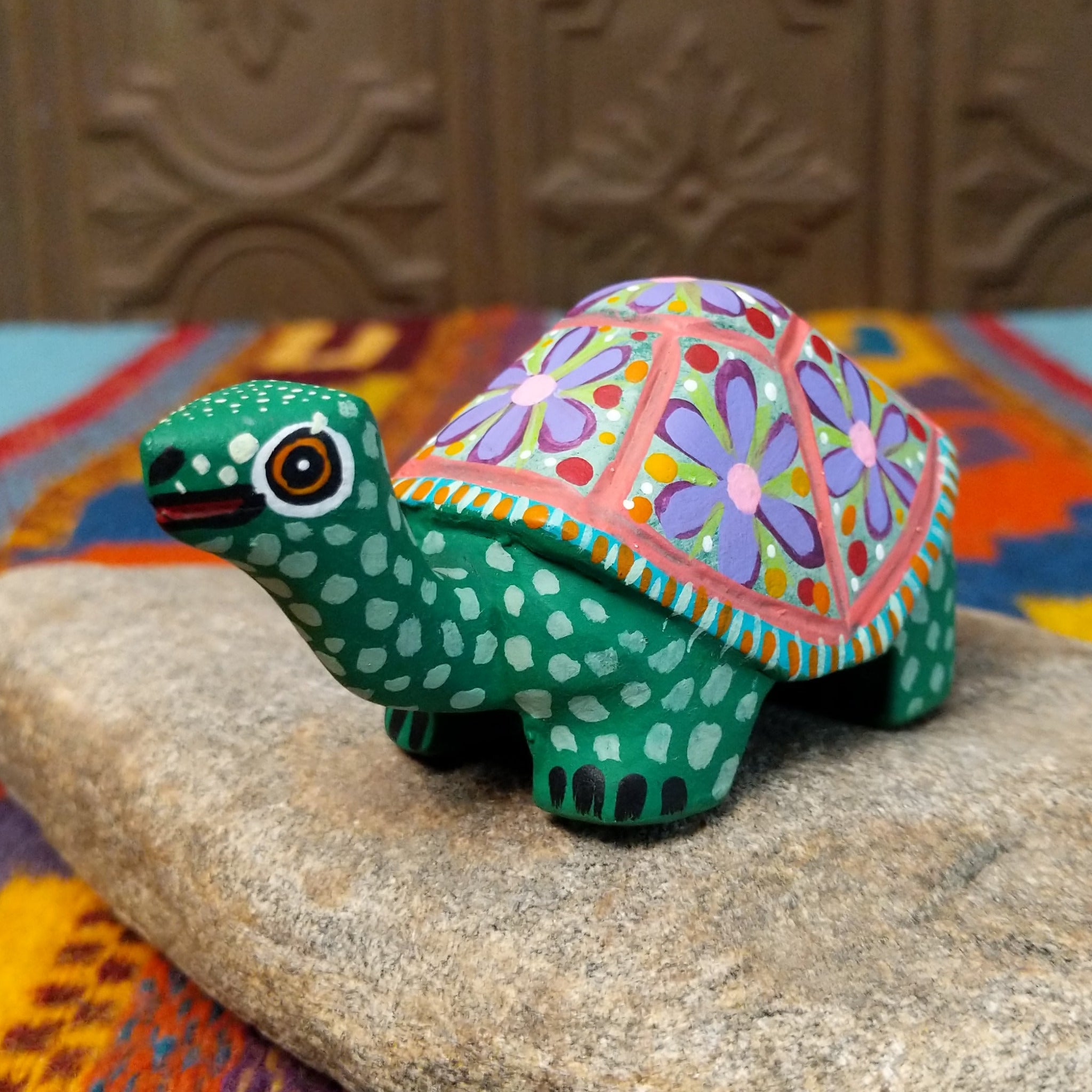 This green Oaxacan tortoise wood carving by Rosaura Ortega features a domed shell decorated with purple flowers, pink borders, and colorful hand-painted dots and patterns.