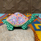 This green Oaxacan tortoise wood carving by Rosaura Ortega features a domed shell decorated with purple flowers, pink borders, and colorful hand-painted dots and patterns; side view.