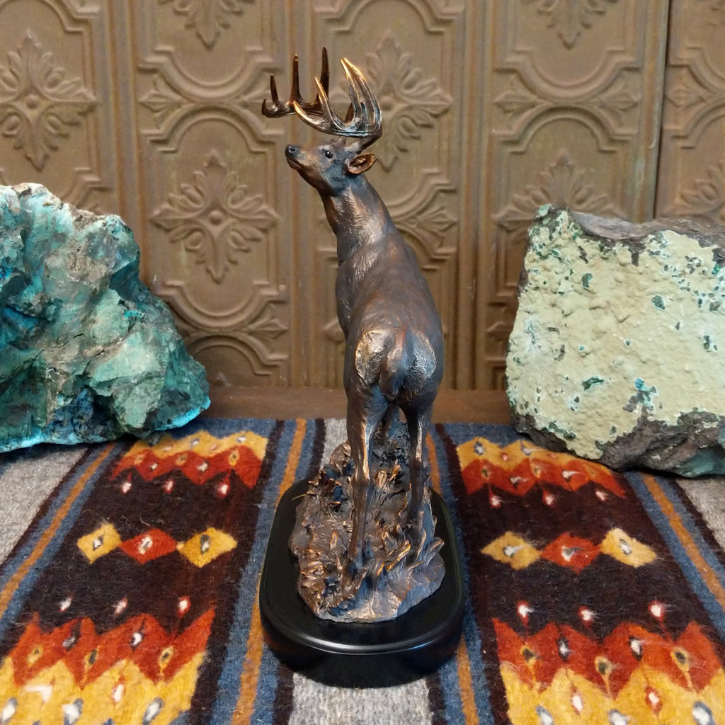 Sculpture showing a bronze deer with large antlers standing proudly on a textured base.