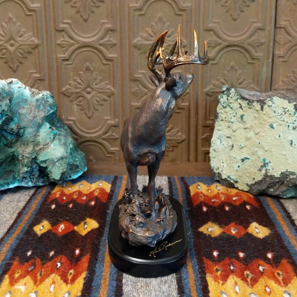 Sculpture showing a bronze deer with large antlers standing proudly on a textured base.
