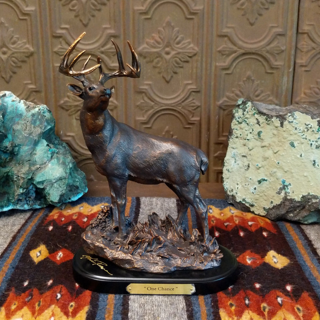 Sculpture showing a bronze deer with large antlers standing proudly on a textured base.