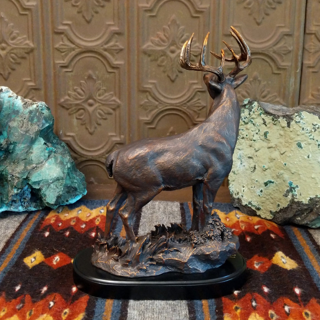 Sculpture showing a bronze deer with large antlers standing proudly on a textured base.