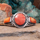 A sterling silver cuff features a central red spiny oyster shell stone and two orange spiny oyster shell pieces in notched bezels with twisted silver rope.
