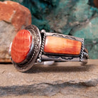 The side of the cuff shows the notched bezel with red and orange spiny oyster shell, accented by twisted silver rope along the band.