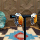 Sterling silver earrings featuring orange spiny oyster shell set in bezels, framed by twisted rope and etched setting.
