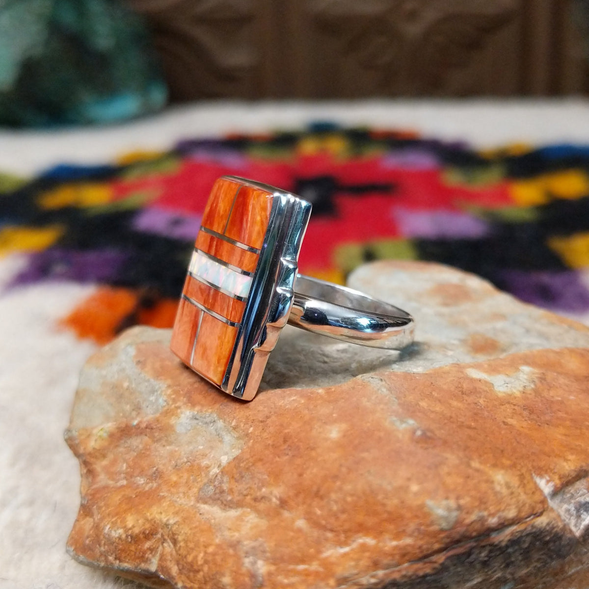 Orange spiny oyster shell inlay ring by Raymond Coriz with a central opal strip and rectangular silver setting.