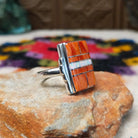Orange spiny oyster shell inlay ring by Raymond Coriz with a central opal strip and rectangular silver setting.
