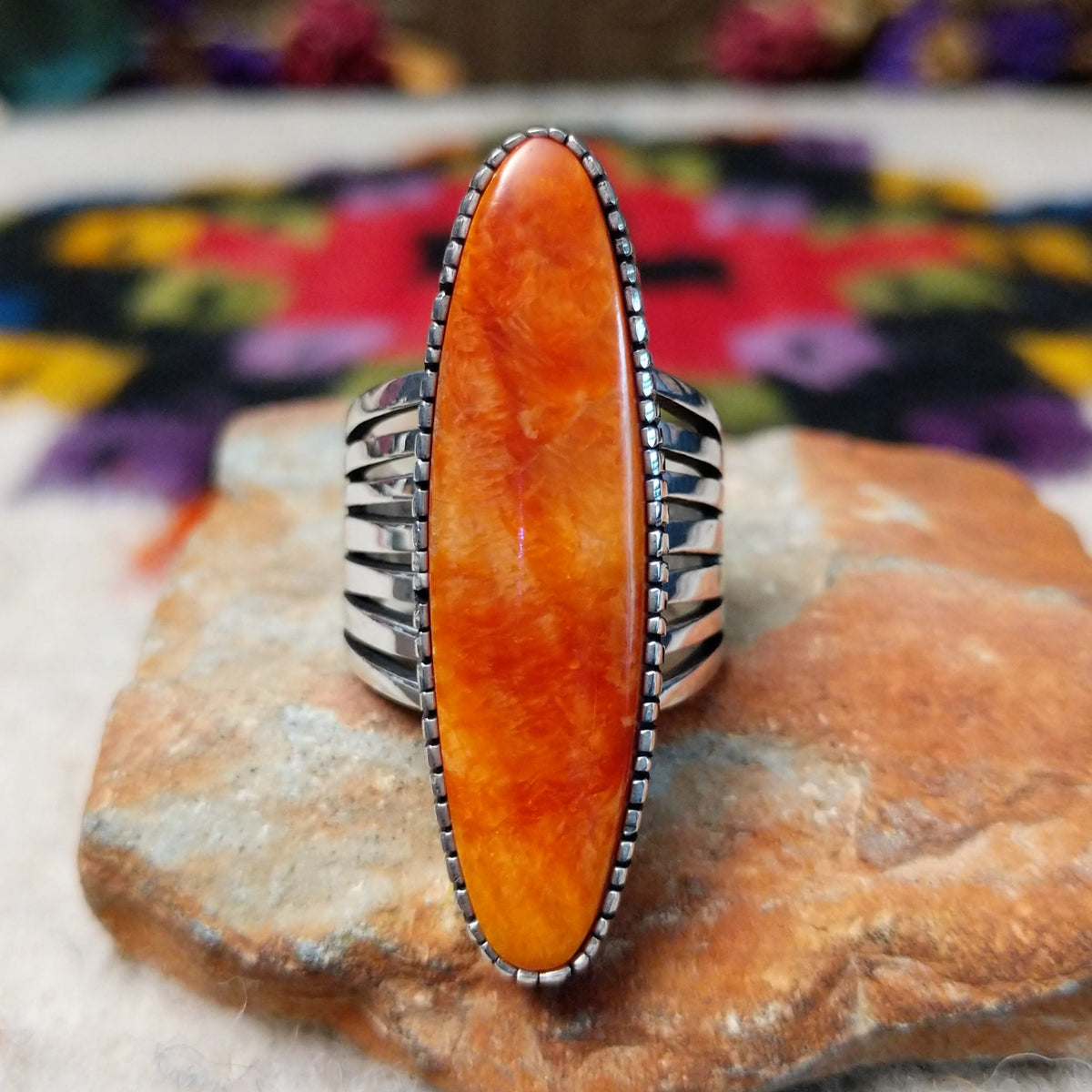 Orange Spiny Oyster Shell Navette Ring by Bernyse Chavez with an elongated orange and red shell cabochon, detailed sterling silver bezel, and wide split-style band.