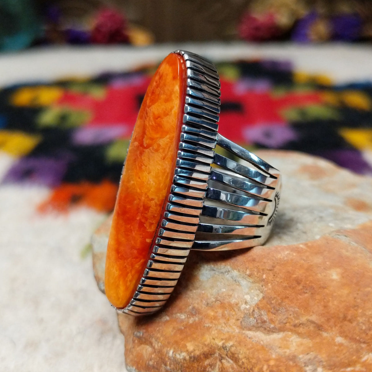 Orange Spiny Oyster Shell Navette Ring by Bernyse Chavez with an elongated orange and red shell cabochon, detailed sterling silver bezel, and wide split-style band; side view.