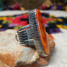 Orange Spiny Oyster Shell Navette Ring by Bernyse Chavez with an elongated orange and red shell cabochon, detailed sterling silver bezel, and wide split-style band; side view.