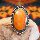 Sterling silver ring with oval orange spiny oyster shell set in the bezel, framed by twisted rope and dotted accents.