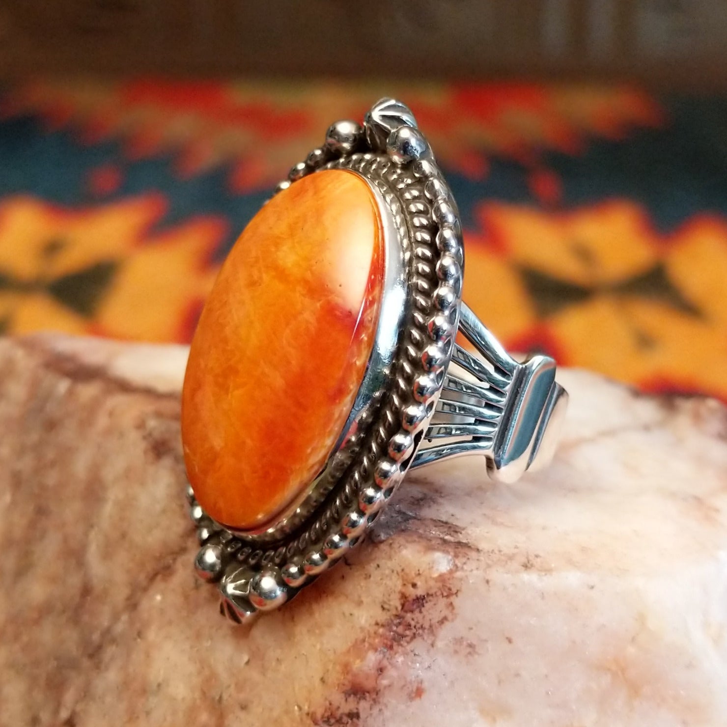 Sterling silver ring with oval orange spiny oyster shell set in the bezel, framed by twisted rope and dotted accents.