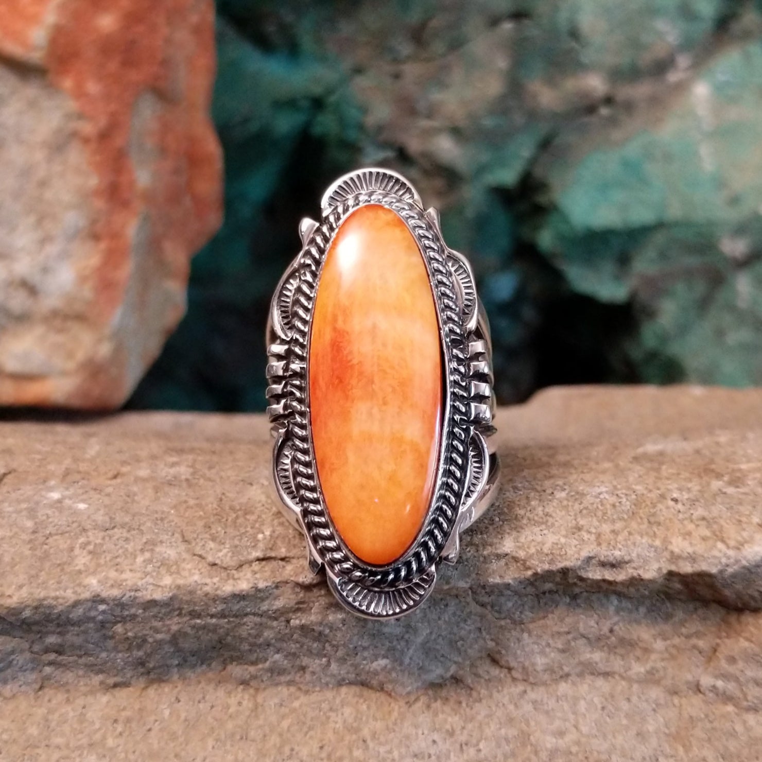 A sterling silver ring features an orange spiny oyster shell stone in a smooth bezel with twisted silver rope detailing.