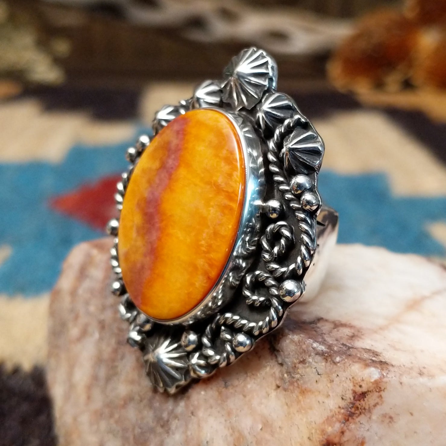 Sterling silver ring with orange spiny oyster shell set in the bezel, framed by ornate silverwork.