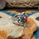 Handcrafted Navajo sterling silver ring by Raymond Coriz featuring an oval red coral cabochon surrounded by twisted rope, silver bead accents, and an ornate openwork floral design; side view.