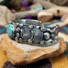Handcrafted sterling silver cuff by Andrew Gordon featuring a Kingman turquoise cabochon with a twisted rope bezel, surrounded by ornate conchos, fan motifs, silver beadwork, and hand-stamped Southwestern details; side view.